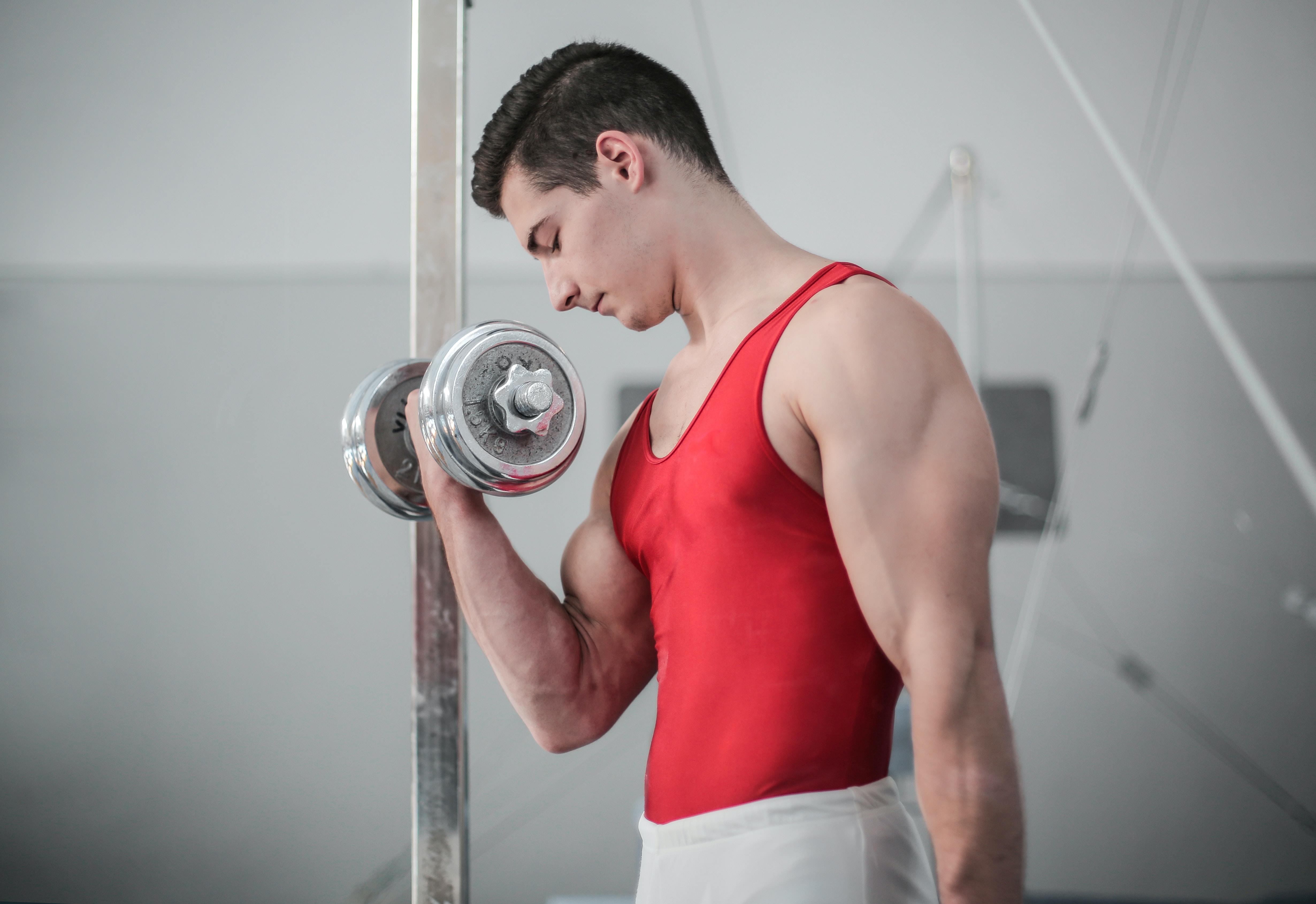 Muž gymnasta posiluje bicepsy jednoruční činkou.